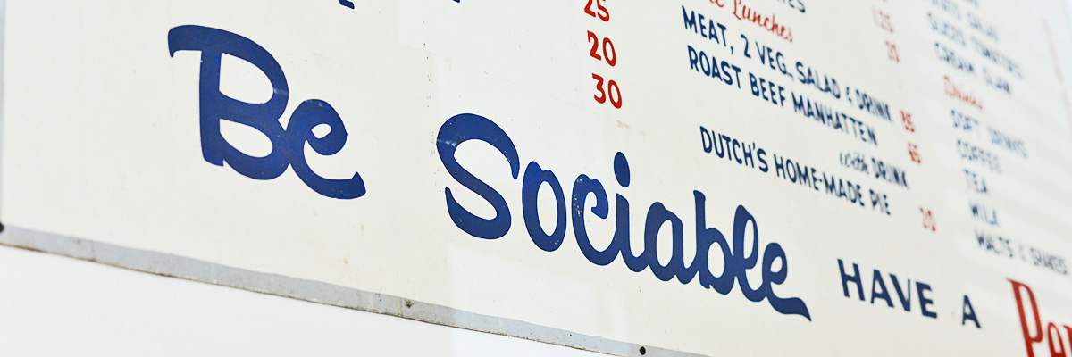 Close up of the old Dutch Cafe sign hanging the community corner of the store. The photo shows a close up of the words, "Be Sociable."